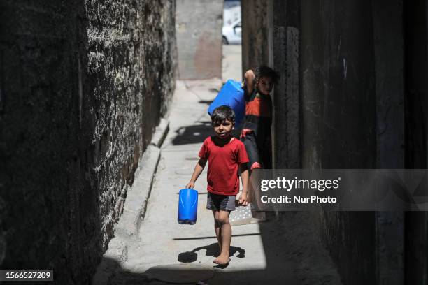 Palestinian children walk with a fresh water jerrycan outside their home amid a heatwave and lengthy power cuts at Shati refugee camp in Gaza City,...