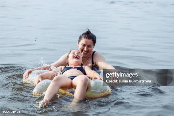 mother with smile full of happiness looking at laughing daughter who lying on rubber ring in form of star and pushing floatie on water. - woman rubber ring stock pictures, royalty-free photos & images