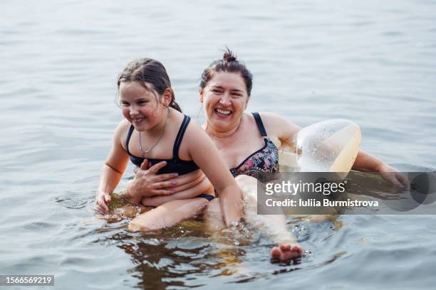 joyful daughter sitting on lap of happy mother, swimming together in star shaped rubber ring in river. - woman rubber ring stock pictures, royalty-free photos & images