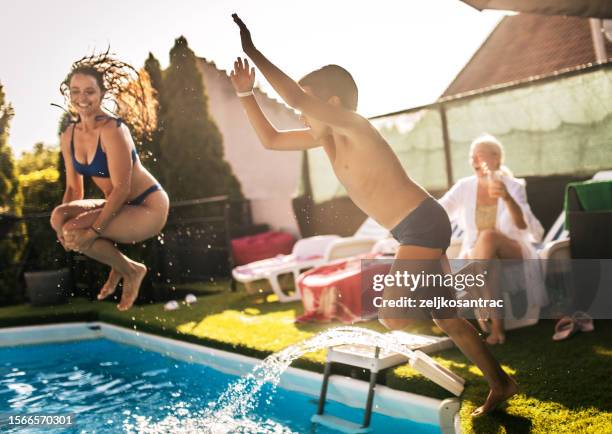 multi generation family enjoying at pool party at home - young girl jumping into swimming pool stock pictures, royalty-free photos & images