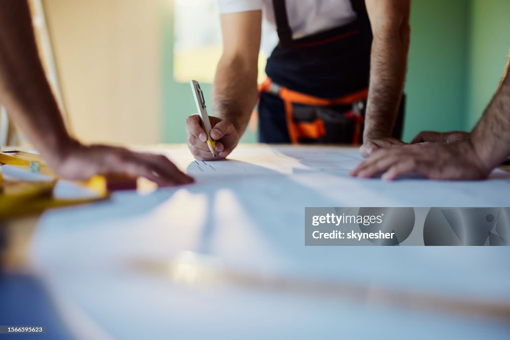 Team of unrecognizable workers working on plans at construction site.