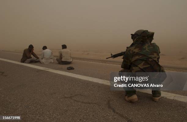 The War In Iraq: Logbook Of 41th Infantry. Les arrestations : civils irakiens assis sur une route sous la surveillance d'un militaire américain les...