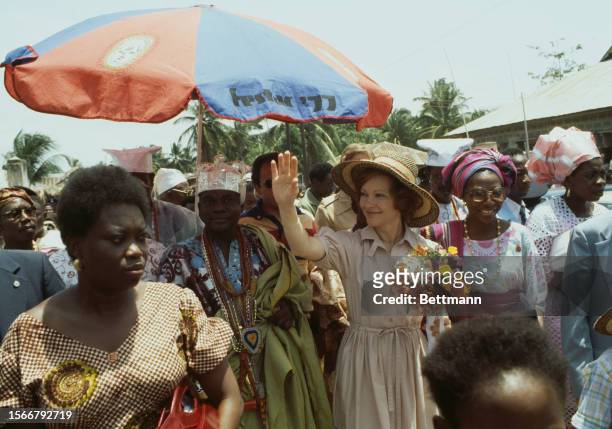 First Lady Rosalynn Carter waves as she walks through the village of Badagry, near Lagos, during a visit to Nigeria, April 2nd 1978. Escorting her is...