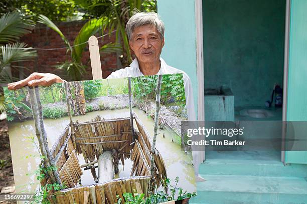 Nguyen Van Tu displays a picture of his old toilet as he poses in front of his newly installed toilet as part of a media briefing for World Toilet...