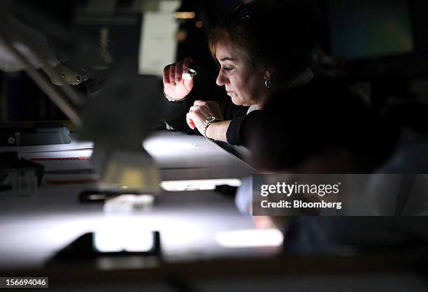 An employee sits at a sorting table and uses magnifying glass to sort uncut diamonds at the De Beers office in London, U.K., on Friday, Nov. 16,...