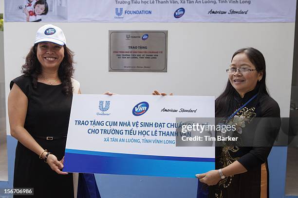 Marketing Vice President of Unilever Vietnam Nguyen Thi Bich Van and Principal of Le Thanh Van Primary School Ha Thi Dung hold a cheque at the...