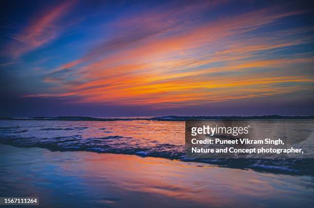 a dramatic cloud formation and deep vibrant colours formed during sunset at a beach near surat, gujarat, india. - gujarat stock photos et images de collection