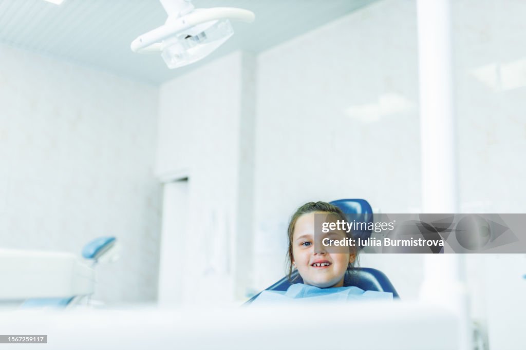 Happy little girl sitting in dentistry cabinet, looking at camera and smiling waiting for start of bridle cutting surgery.