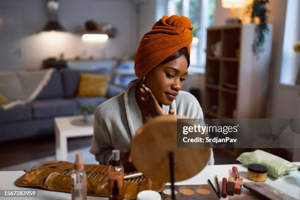 woman of black ethnicity, looking herself in the mirror, while doing a skin care routine - dark skin tone stock pictures, royalty-free photos & images