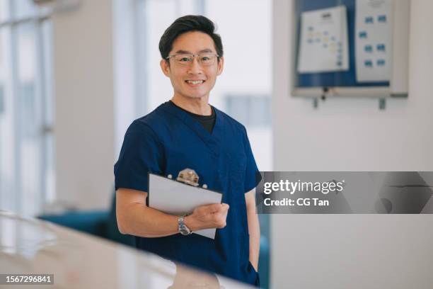 portrait asian male nurse looking at camera smiling standing in front of doctor's office - physical therapist stock pictures, royalty-free photos & images
