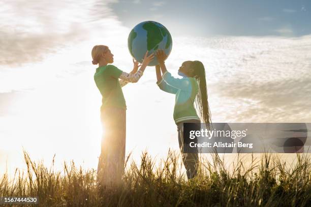 two female eco activists holding up a hand painted globe - sustainable development goals stock pictures, royalty-free photos & images