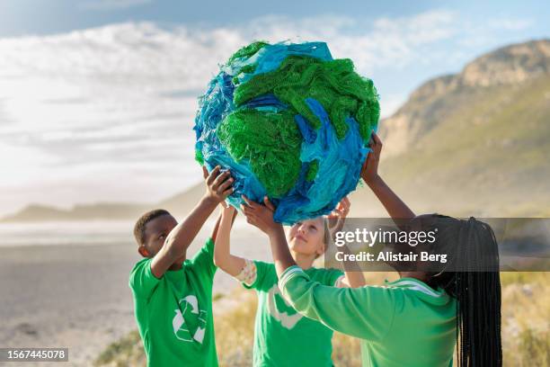 group of young climate activists holding up a globe together by the sea - umweltaktivist stock-fotos und bilder