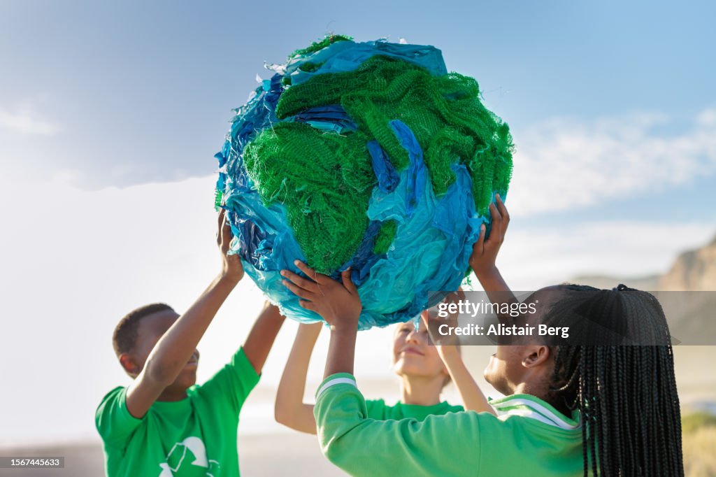 Group of young climate activists holding up a globe together by the sea