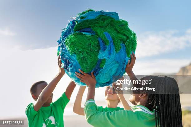 group of young climate activists holding up a globe together by the sea - umweltaktivist stock-fotos und bilder