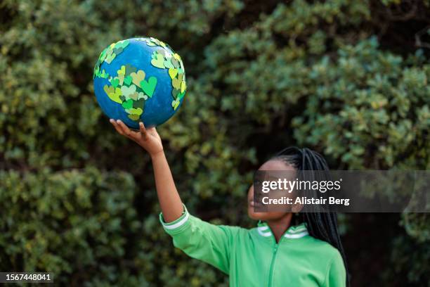 young african girl holding up a homemade globe of green heart shapes - ragazza scuola foto e immagini stock