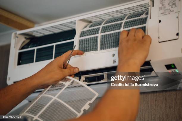 unrecognizable man returning new, cleaned filters back to air conditioner hanging on wall after purifying. - airconditioning stockfoto's en -beelden