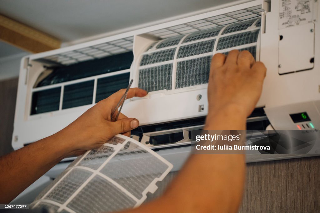 Unrecognizable man returning new, cleaned filters back to air conditioner hanging on wall after purifying.