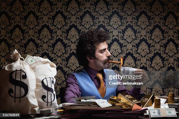 adult man sitting lighting cigar with burnt dollar bill - millionnaire stock pictures, royalty-free photos & images