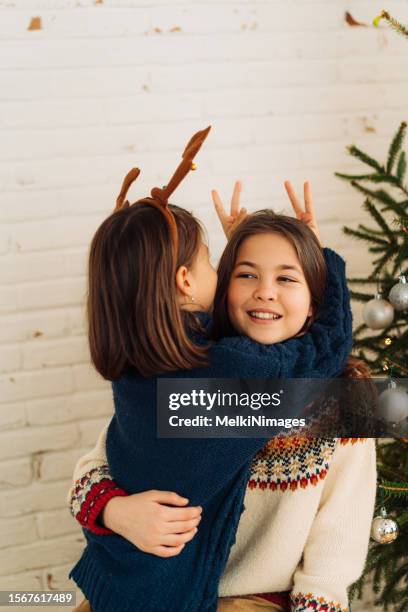 two girls having fun embracing in front of christmas tree - sibling christmas stock pictures, royalty-free photos & images