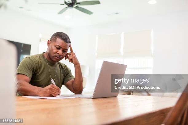 male soldier sits at his dining room table to work on the computer during his lunch break - veteran entrepreneur stock pictures, royalty-free photos & images