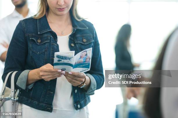 unrecognizable woman reading bank brochure waits in line - blank pamphlet stock pictures, royalty-free photos & images