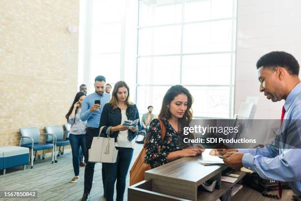 as line grows, bank teller counts woman's cash withdrawal - bank teller stock pictures, royalty-free photos & images