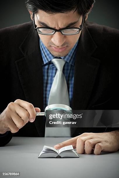 businessman looking in a miniature book through magnifying glass - little effort stock pictures, royalty-free photos & images