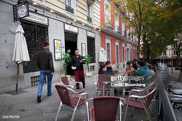 An employee delivers plates of food to customers sitting on an outdoor terrace outside a 100 Montaditos restaurant in Madrid, Spain, on Wednesday,...