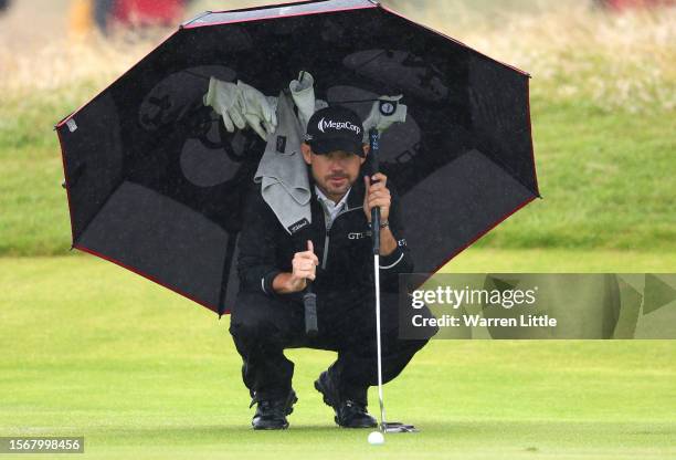 Brian Harman of the United States looks on from under his umbrella surrounded by gloves as he keeps dry from the rain during the final round of The...