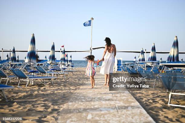 famiglia felice che corre sulla spiaggia in una giornata estiva. - ombrellone da spiaggia foto e immagini stock
