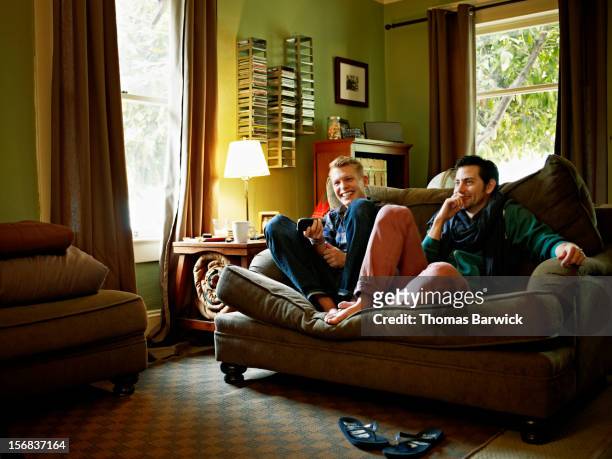 gay couple sitting on couch in home watching tv - sofa stock-fotos und bilder