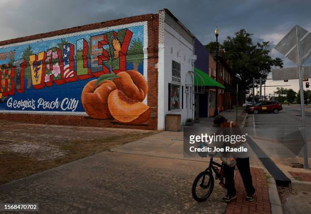 Bicyclist walks past a mural declaring the town "Georgia's Peach City" on July 24, 2023 in Fort Valley, Georgia. Peach farmers in Georgia say that a...