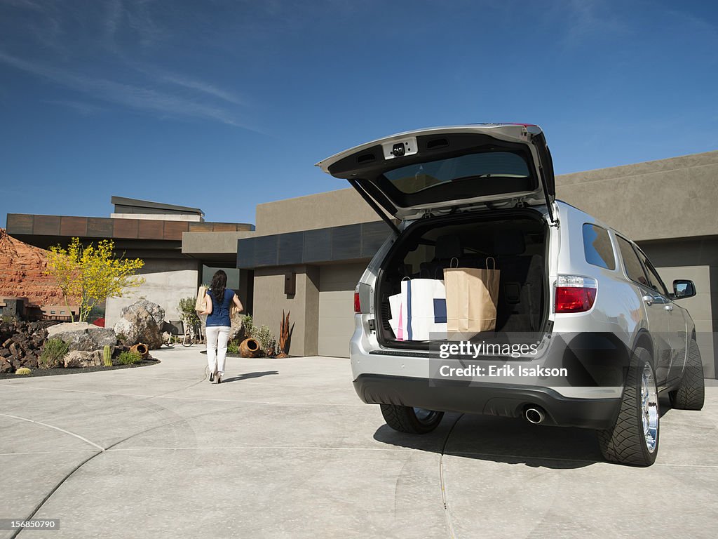 USA, Utah, St. George, Young woman unpacking shopping from car parked in yard