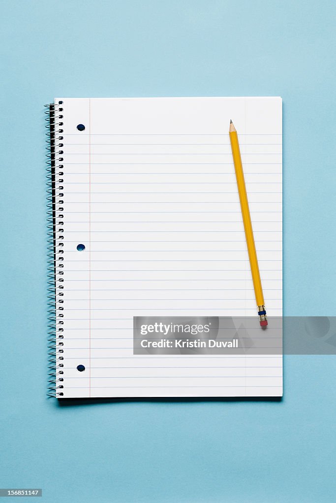 Single yellow sharpened pencil with blank spiral notebook on blue background