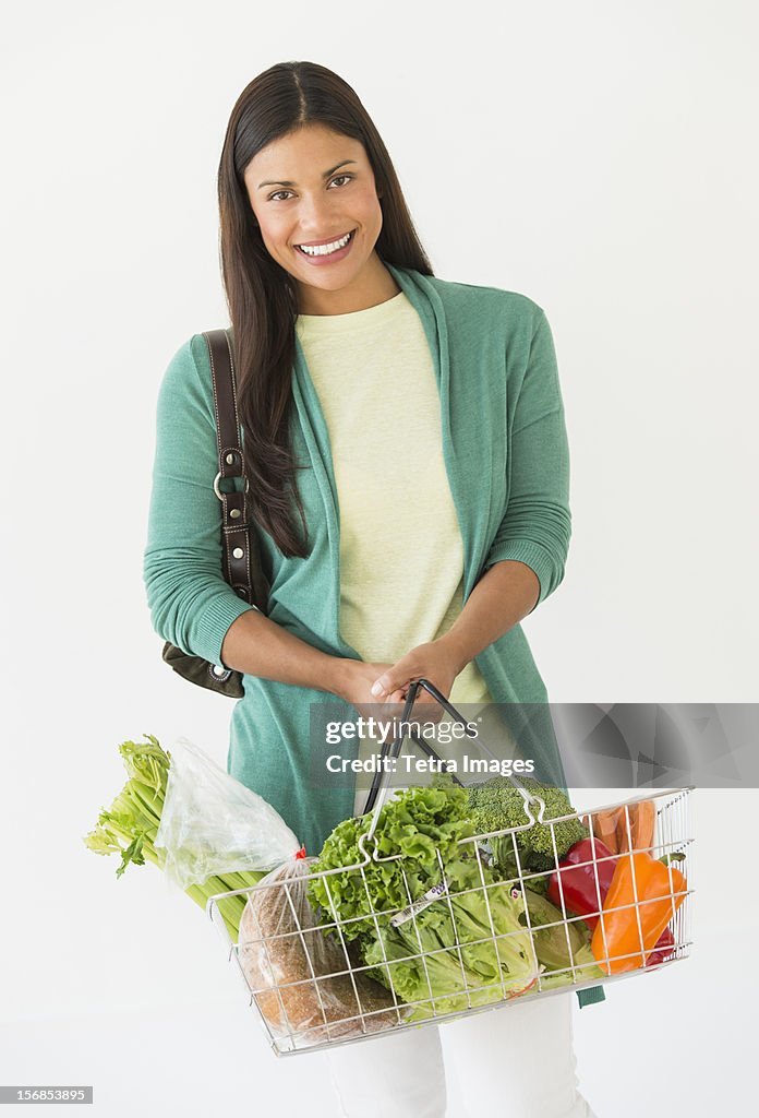 Studio shot of woman holding shopping basket with vegetables