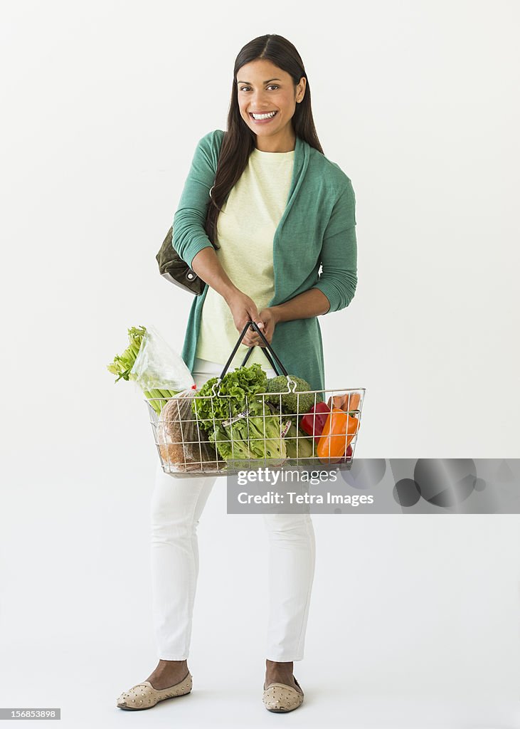 Studio shot of woman holding shopping basket with vegetables