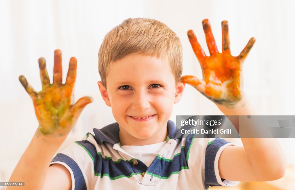 Young boy (6-7) showing hands stained with paint