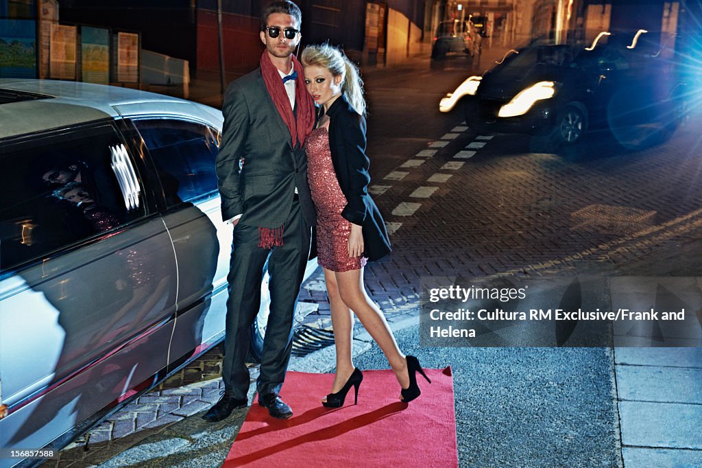 Couple posing on red carpet by limousine