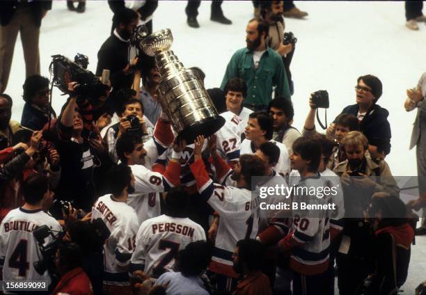 Clark Gillies of the New York Islanders hands the Stanley Cup Trophy to teammate Greg Gilbert after defeating the Edmonton Oilers in Game 4 of the...