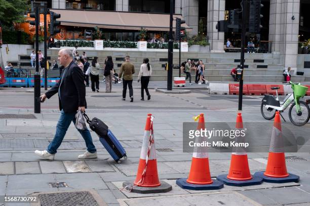 Four traffic cones stand on an uneven surface where maintenance covers make a trip hazard on the pavement as a warning for pedestrians to avoid on...