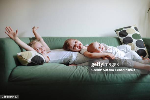 capturing childhood: genuine sibling love and happy displayed on green sofa - three people on couch stock pictures, royalty-free photos & images