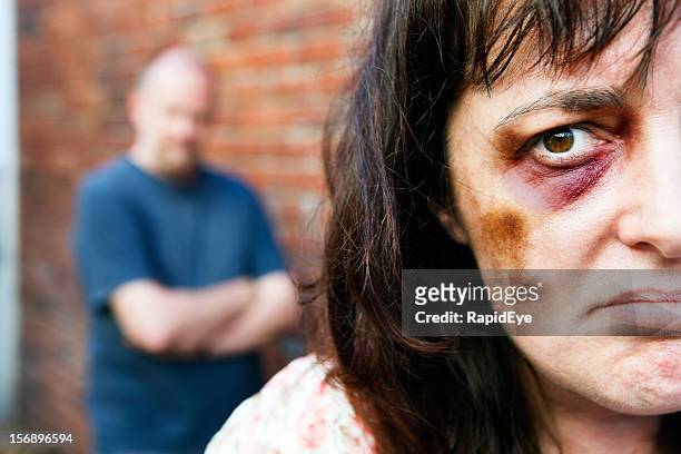 despairing battered woman with threatening male in background - rea001 stock pictures, royalty-free photos & images