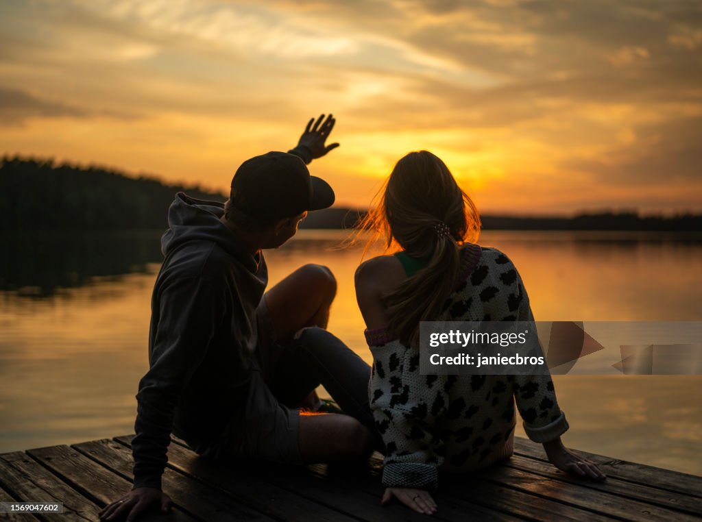 Romantic couple relaxing on the pier. Enjoying the scenery of sunset at lake together