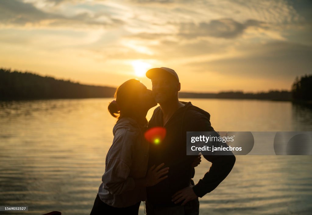 Romantic couple relaxing by a lake. Enjoying the scenery of sunset and kissing