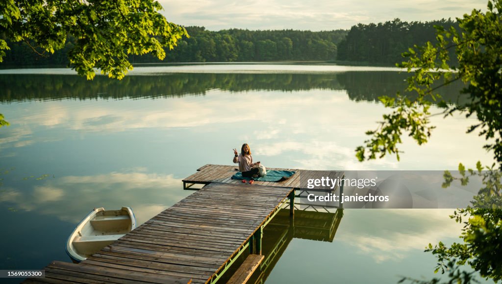Woman relaxing on a wooden pier. Watching the calm water surface with clouds reflecting