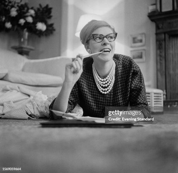 British fashion designer Belinda Bellville lying on the floor and chewing a pencil, February 9th 1960.