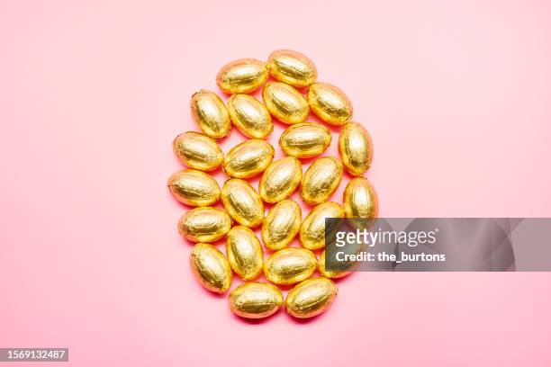 high angle view of golden chocolate easter eggs on pink background - chocolate foil stock pictures, royalty-free photos & images