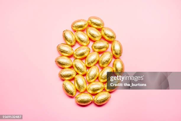 high angle view of golden chocolate easter eggs on pink background - tin foil costume - fotografias e filmes do acervo