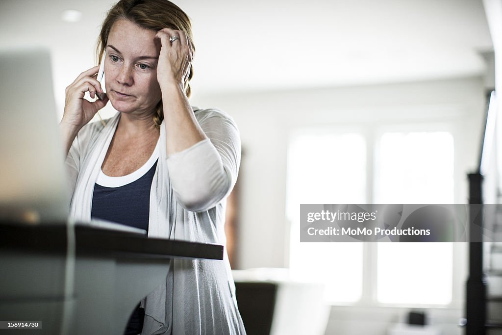Woman on smartphone looking at laptop