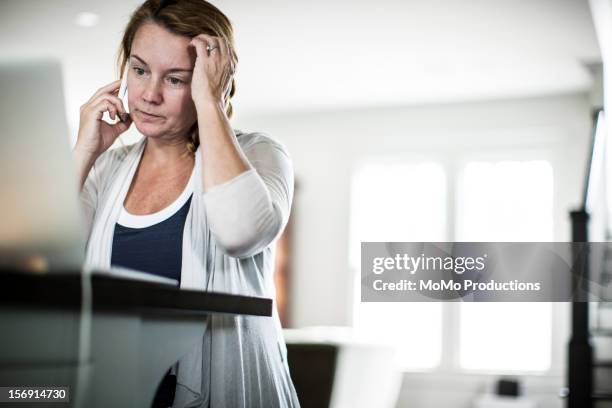 woman on smartphone looking at laptop - telephone hotline stock pictures, royalty-free photos & images